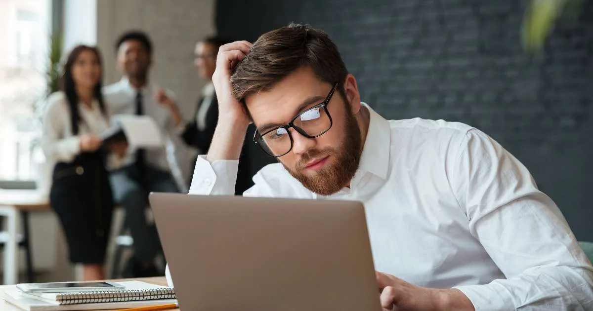 Hombre revisando en la laptop por qué no llegan prospectos, con su equipo al fondo.