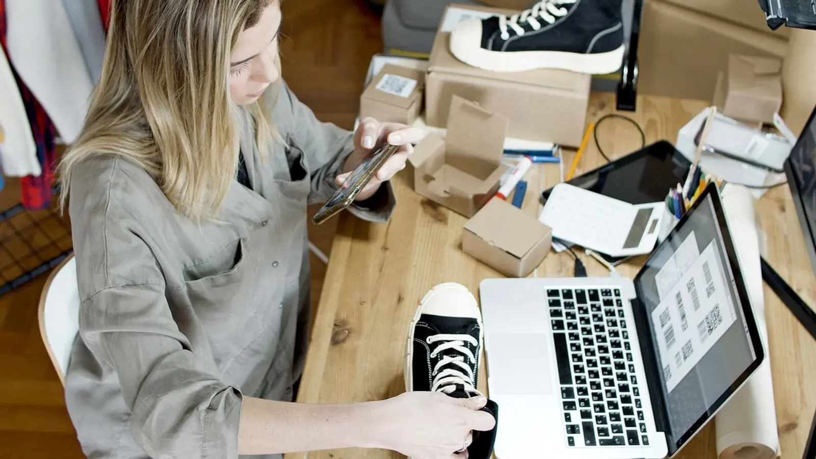 Mujer fotografiando un tenis junto a cajas, para publicarlo en su tienda.